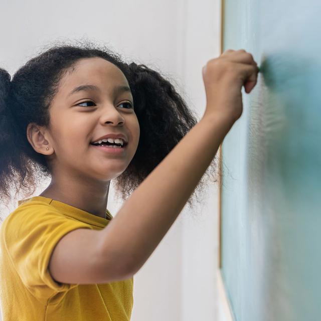 young girl writing on chalkboard in classroom